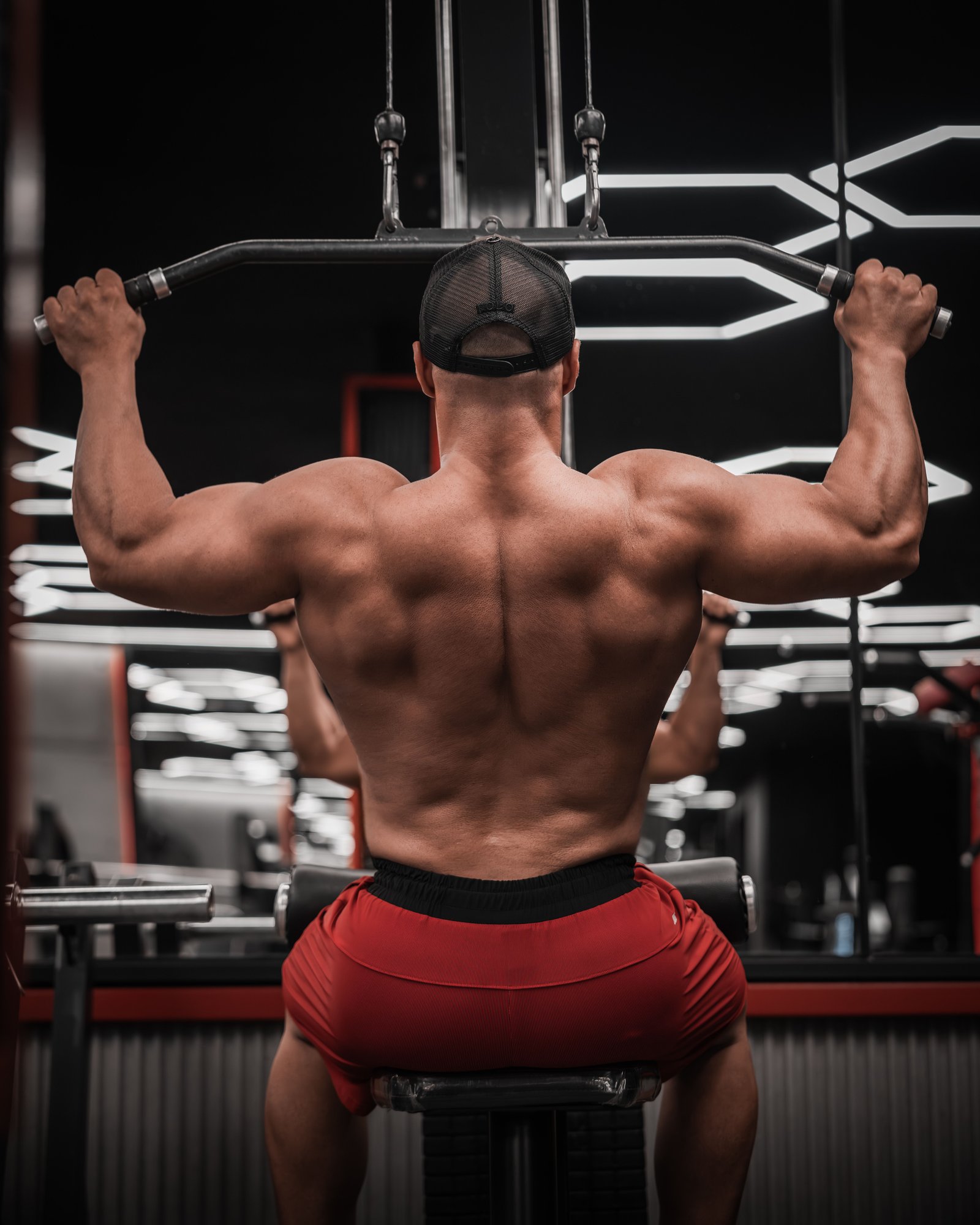 Muscular man performing lat pulldown exercise in a well-equipped gym.