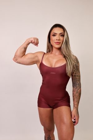 Athletic woman showing strength with bicep pose in maroon bodysuit.